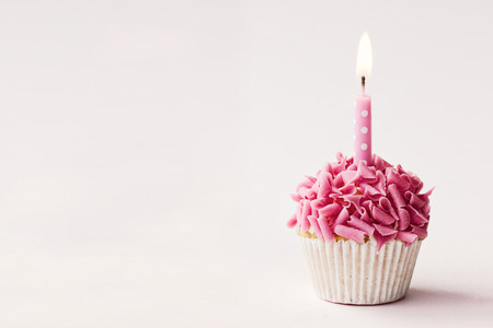 Cupcake decorated with pink chocolate curls and a single candleの写真素材
