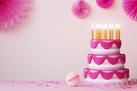 Birthday party with pink tiered birthday cake and golden candlesの写真素材