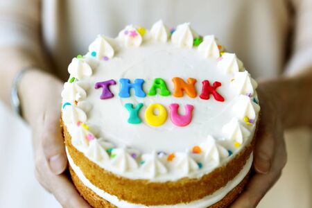 Hands holding cake with colorful rainbow letters spelling thank youの写真素材