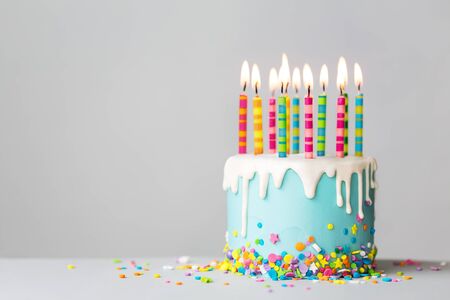 Birthday cake with white drip icing, sprinkles and colorful birthday candlesの写真素材