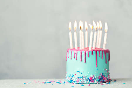 Birthday cake with blue frosting, pink drip icing and ten white birthday candlesの写真素材