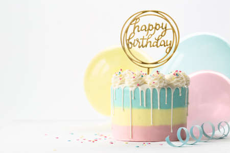 Pastel birthday cake with drip icing and balloonsの写真素材