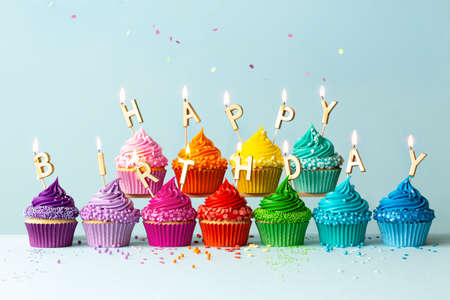 Rainbow colored cupcakes with birthday candles spelling happy birthdayの写真素材