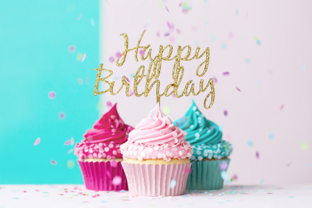 Pink and blue birthday cupcakes with happy birthday sign and confettiの写真素材