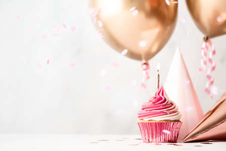 Birthday celebration with pink birthday cupcake, party hats and rose gold balloonsの写真素材