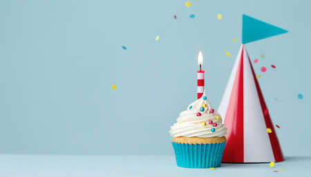 Birthday cupcake with one birthday candle and red and white striped party hatの写真素材