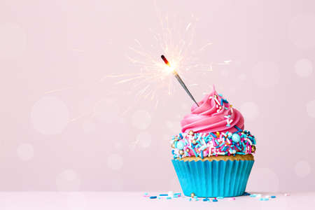 Birthday cupcake with celebration sparkler and colorful pink and blue sugar sprinklesの写真素材