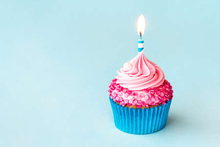 Celebration birthday cupcake with striped birthday candle and pink sprinkles on a blue backgroundの写真素材