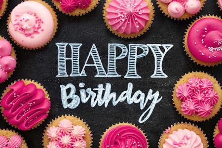 Overhead view of pink birthday cupcakes arranged on a chalkboard with happy birthday greeting written in chalkの写真素材