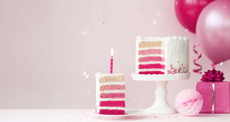 Pink ombre birthday cake with balloons and slice of birthday cake and candleの写真素材