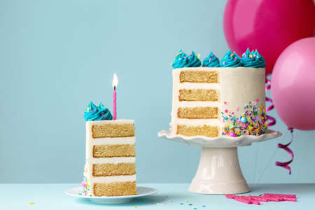 Birthday cake with layers and turquoise frosting, slice removed and one pink birthday candleの写真素材