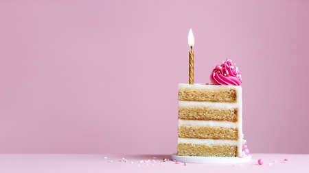 Slice of birthday cake with gold birthday cake candle and pink frosting on a pink backgroundの写真素材