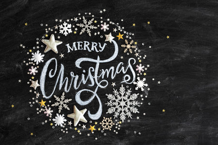 Merry Christmas written in chalk on a black chalkboard with confetti and Christmas decorations, flat lay viewed from aboveの写真素材