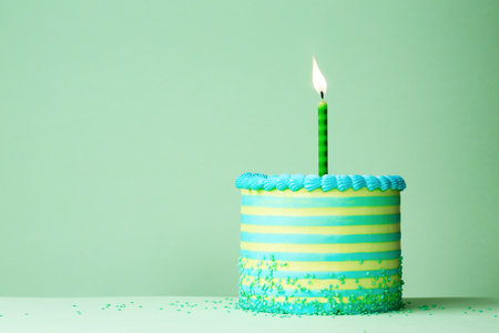 Green and blue striped birthday cake with one celebration birthday candle against a plain green backgroundの写真素材