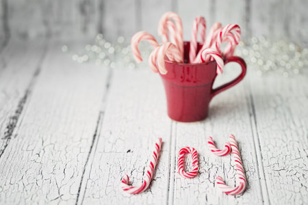 Red mug filled with candy canes spelling joy on a white background