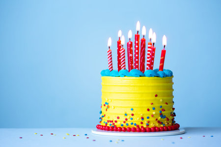 Colorful celebration birthday cake with yellow frosting and red birthday candles against a blue...