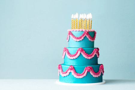 Tiered celebration birthday cake with pink ornate piped buttercream frills and gold birthday candlesの写真素材