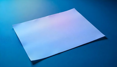 Blank white sheet of paper on textured dark surface illuminated by warm lightの素材