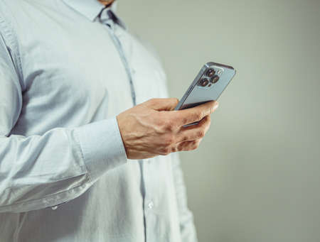 man in a shirt holding smartphones and checking and typing messages. on a one-color backgroundの写真素材