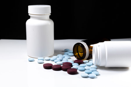 two plastic bottles and one glass with colored pills on a white table with a black background....