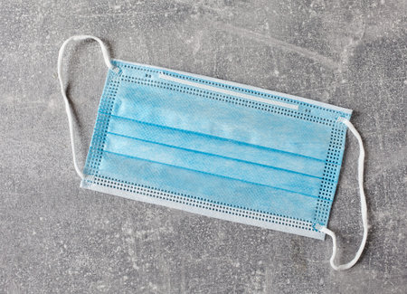 blue medical face mask on gray table, top view