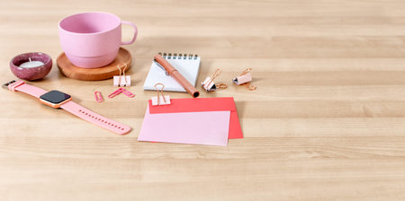Office desk with tea cup, notebook, pen, card and envelope. Wooden desktop.