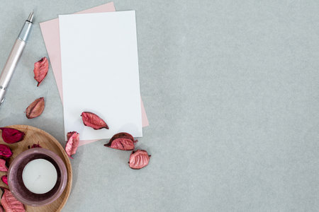 Blank pink and white card with candle and petals, on gray background.の写真素材