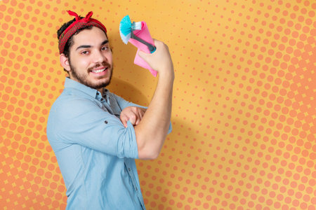 Happy man support feminism holding cloth and cleaning brush, on pop background.