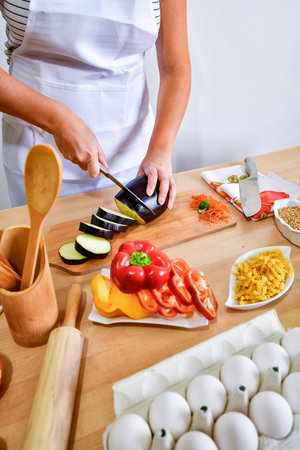 Female cook cutting eggplant on wooden board in kitchen.の写真素材