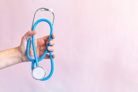 Female hand holds a stethoscope on a light pink isolated background.の写真素材