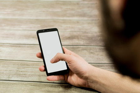 close up of Male hand holding a phone with white screen top view, on wooden table. Communication concept.の写真素材