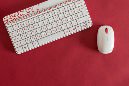 white keyboard and mouse, on red background, with notebook and pen.