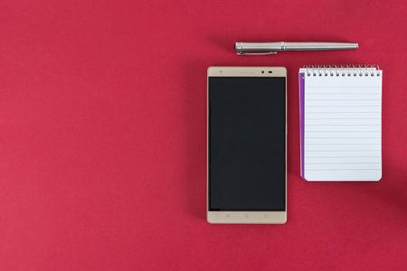 cell phone, notebook and pen, on red background.の写真素材