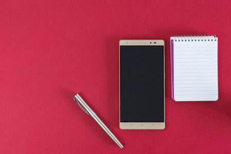 cell phone, notebook and pen, on red background.の写真素材