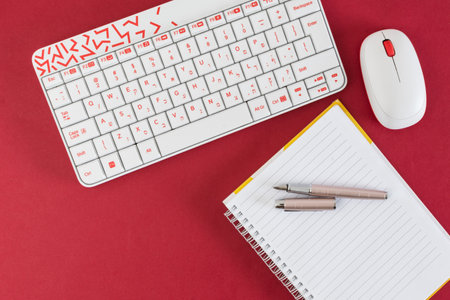 white keyboard and mouse, on red background, with notebook and pen.の写真素材
