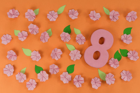 International Women Day. Pink origami flowers with paper green leaves, on orange background. Spring...