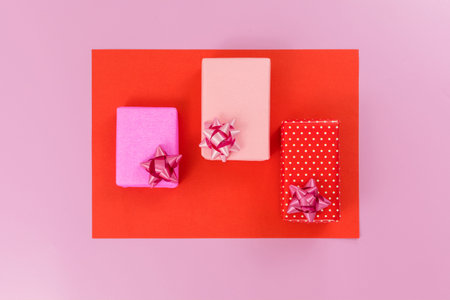 Small gifts, wrapped with pink, red paper, with bow, on pink and red table. top view. selective...