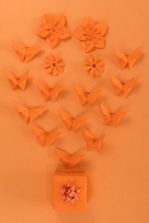 Orange origami butterfly, gift and paper flowers, on orange background. Spring background. top view.の写真素材