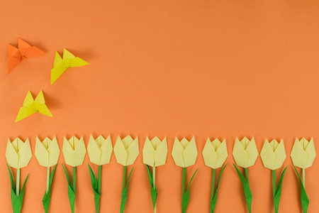 yellow origami tulips and origami butterfly, on orange background. top view. Paper art. Spring background.の写真素材