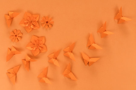 Orange origami butterfly and paper flowers, on orange background. Spring background. top view.の写真素材