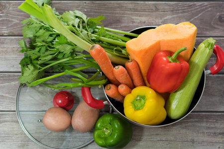 Fresh vegetables coming out of a cooking pot for soup, on wooden table. pumpkin, carrots, celery,...
