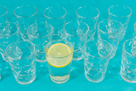 Line of glasses, a glass with water and lemon slice, on a light blue background. Difference conceptの写真素材