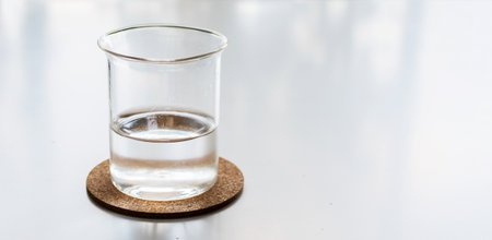 Glass of fresh water, on white desk. Cork coaster.の写真素材