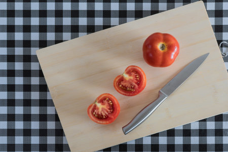 assorted vegetables on wooden board, with knife, on table with black and white checkered tablecloth. tomatoes.の写真素材