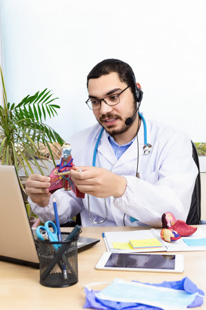 Male doctor talking with colleagues through a video call with a laptop in the consultation.の写真素材