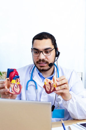 Male doctor talking with colleagues through a video call with a laptop in the consultation.の写真素材