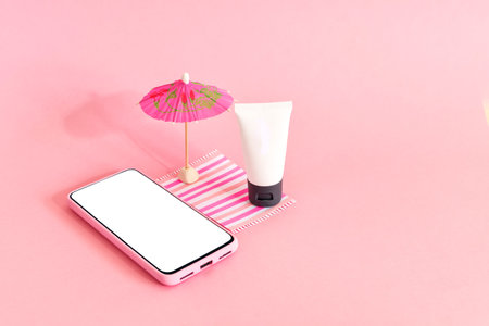 Assembling the skin care cream bottle container, beach umbrella and smart phone on pink background. Summer travel and vacation concept. Beauty and cosmetics concept.の写真素材