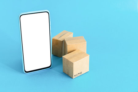 Smart phone with blank screen and cardboard boxes on light blue background. Online shopping and delivery service concept.の写真素材