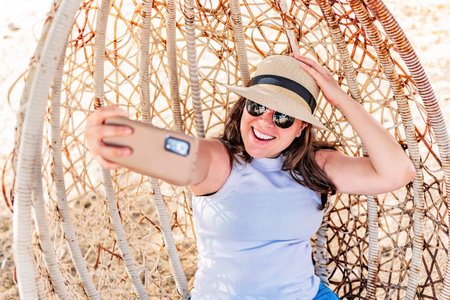 Happy girl sitting in cozy egg swing chair, and taking selfie.