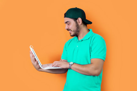 Young bearded man guy in casual t-shirt used tablet, posing isolated on orange background in studio.の写真素材
